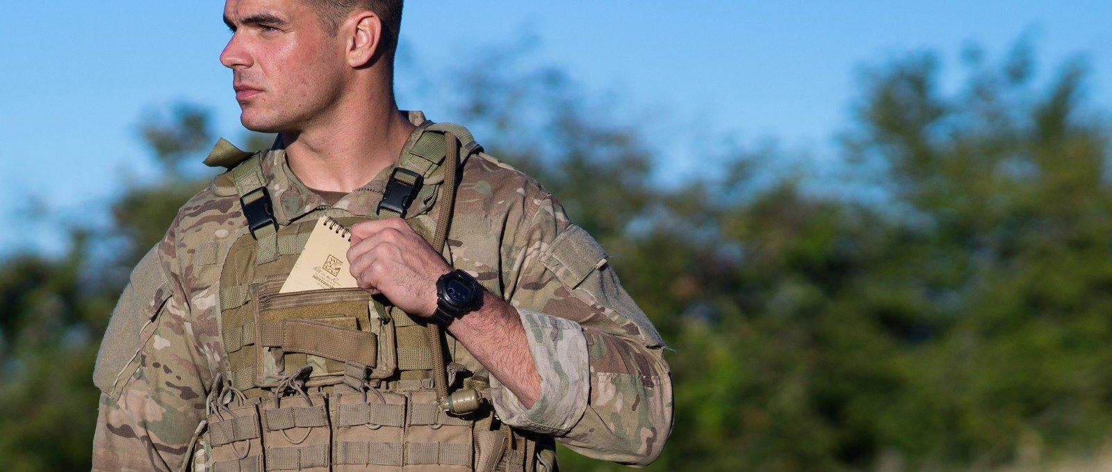 Person in the armed forces putting a notebook into their uniform's pocket.