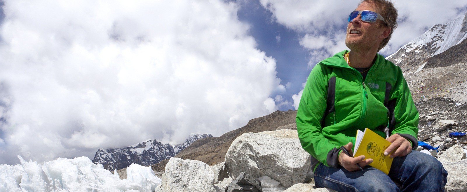 Conrad Anker sitting near a glacier holding the Expedition journal