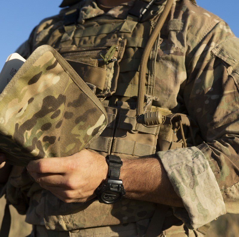 Person in the armed forces holding a multicam cover and field book.