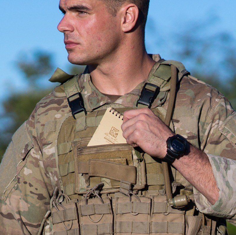 Person in the armed forces putting a notebook into their uniform's pocket.