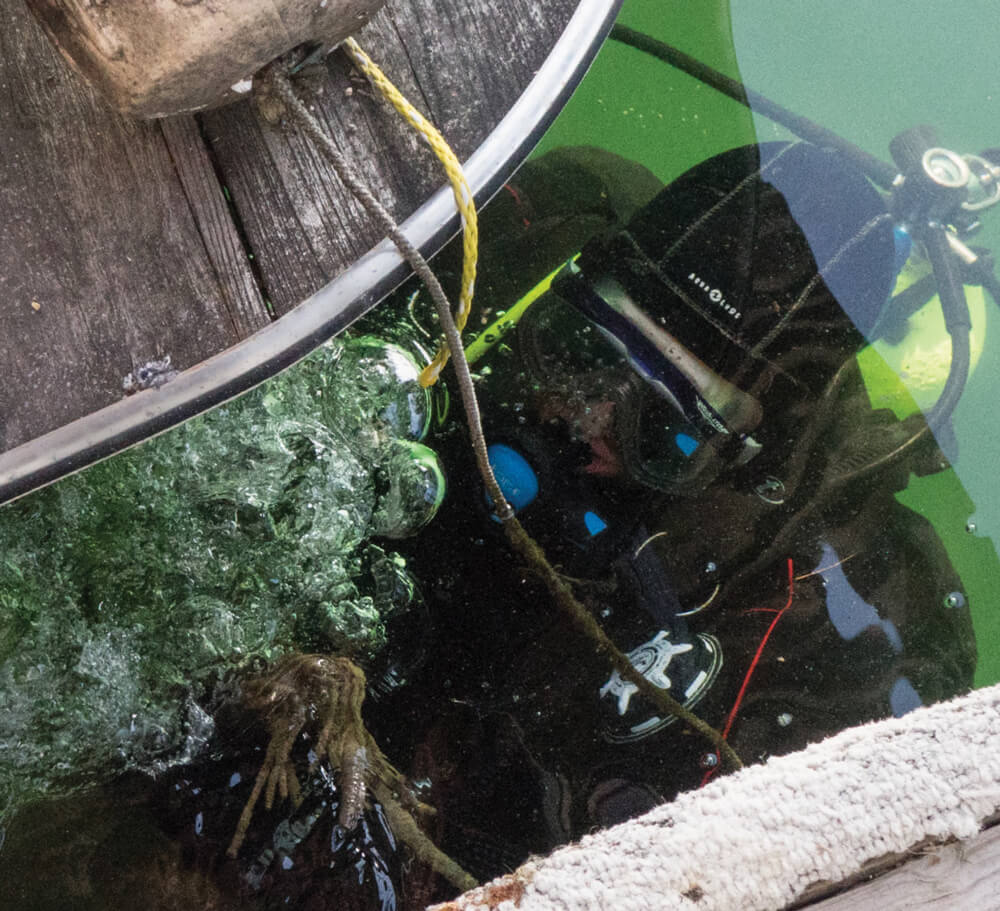 Scuba diver underwater cleaning an engine, bubbles rising.