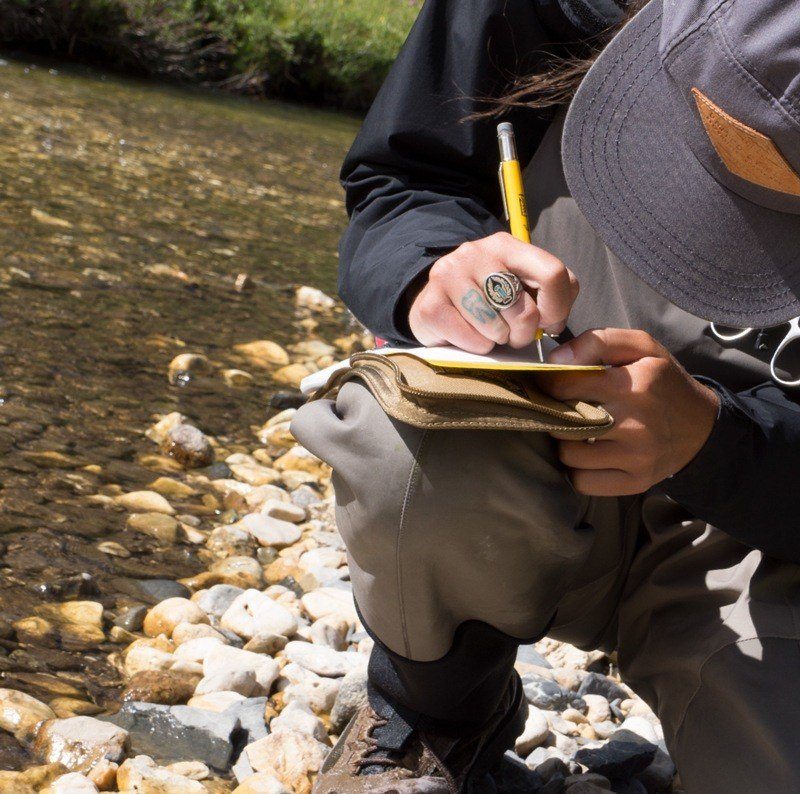 Fishing guide writing in notebook near the river's edge.