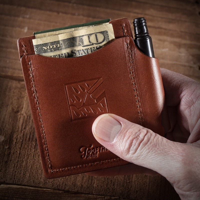 Hand holding wallet, pen in leather loop, ten dollar bill sticking out.